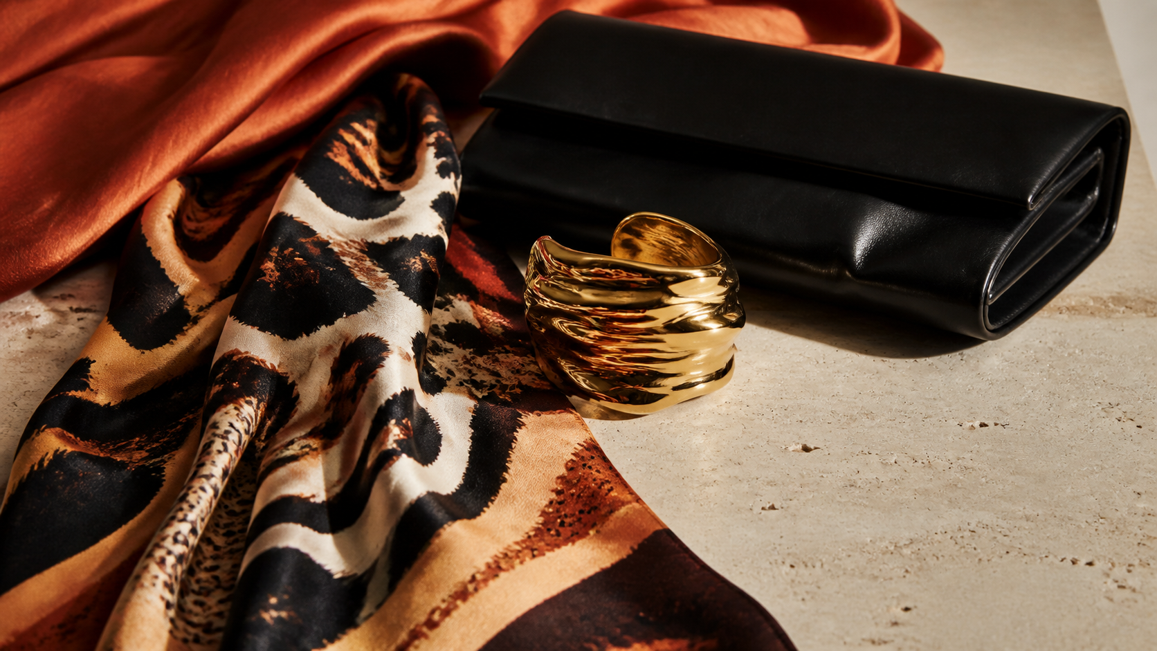 Foulard à motif abstrait, bracelet doré et pochette noire dans une nature morte de mode